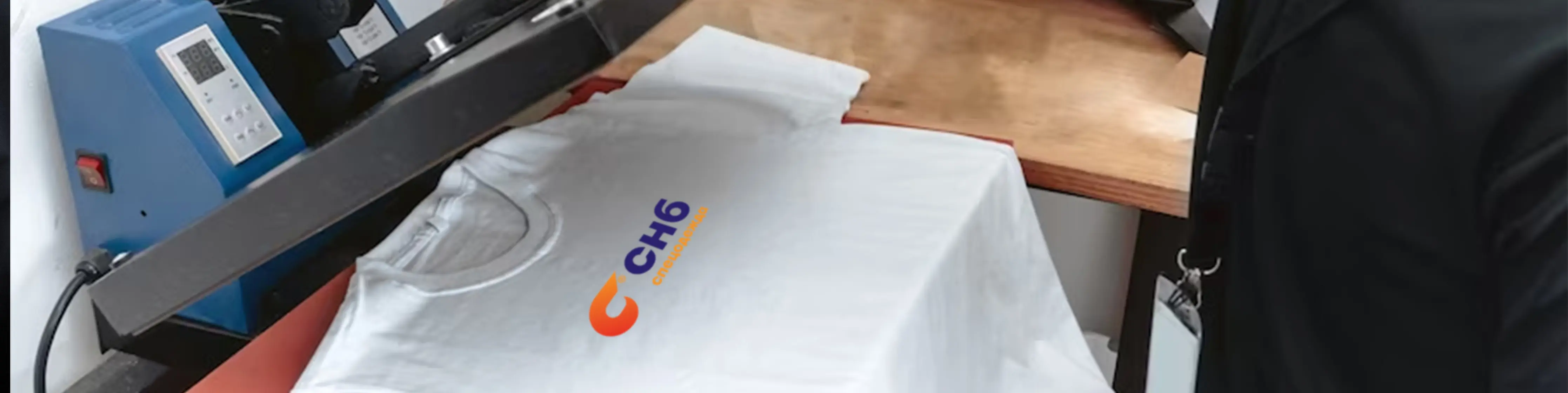 Белая футболка с оранжево-синим логотипом, лежащая на рабочем столе термопресса для печати