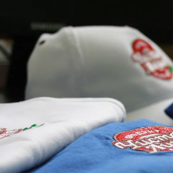 Крупный план белой кепки и синей ткани с вышитыми красными и белыми логотипами, демонстрирующий нанесение фирменной символики на спецодежду