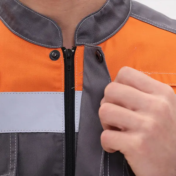 Крупный план человека, застегивающего серо-оранжевую рабочую куртку со светоотражающими полосами. Вдоль швов видны торчащие белые нитки